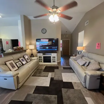 Sale Photo Thumbnail #3: Modern living room setup featuring a pair of off-white leather reclining sofas, a media console with an electric fireplace, a geometric area rug, and framed artwork.