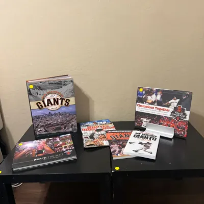 Sale Photo Thumbnail #18: Collection of San Francisco Giants memorabilia books and magazines displayed on small black tables.