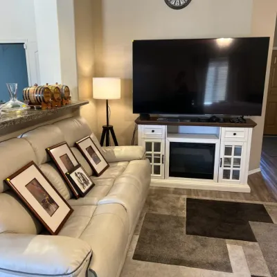 Sale Photo Thumbnail #4: Contemporary living room area featuring a light gray leather reclining sofa, framed wall art, and a large flat-screen TV set on a white media console with an integrated electric fireplace.