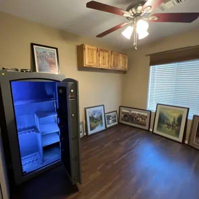 Sale Photo Thumbnail #19: Large steel safe with blue interior LED lighting standing open next to several framed western artwork prints displayed along the walls.