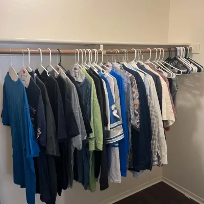 Sale Photo Thumbnail #30: Closet rod filled with various men's shirts, including t-shirts, sports jerseys, and button-down shirts.
