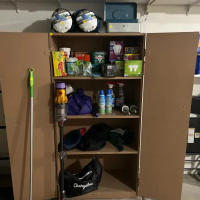 Sale Photo Thumbnail #13: Brown wooden utility cabinet filled with household items, accompanied by a Dyson cordless vacuum cleaner and a green Swiffer floor mop.