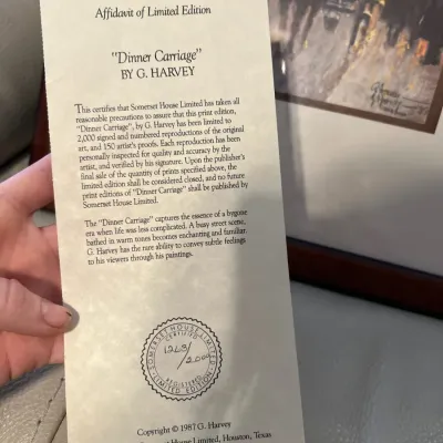 Sale Photo Thumbnail #34: Affidavit of Limited Edition certificate for "Dinner Carriage" by G. Harvey, numbered 1263/2000, dated 1987, shown in front of the framed print.