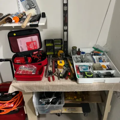 Sale Photo Thumbnail #12: A wooden workbench arranged with various hand and power tools, including a Milwaukee cordless drill kit, Craftsman level, tape measures, pliers, and assorted hardware organizers.