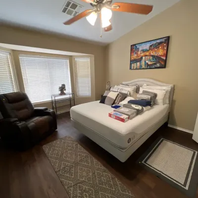 Sale Photo Thumbnail #16: Bedroom featuring a modern Sleep Number mattress on an upholstered frame, accompanied by a leather recliner, area rugs, and a wall painting.