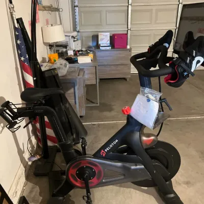 Sale Photo Thumbnail #39: Peloton stationary exercise bike with attached touchscreen monitor, complete with cycling shoes hanging on the handlebars.