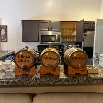 Sale Photo Thumbnail #22: Trio of mini wooden oak aging barrels with spigots and stands, customized with stenciled text on the front.