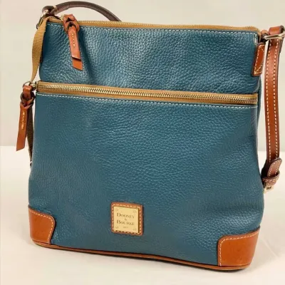 Dooney & Bourke teal blue pebbled leather crossbody bag with tan leather trim, gold-tone hardware logo plate, and front zip pocket.