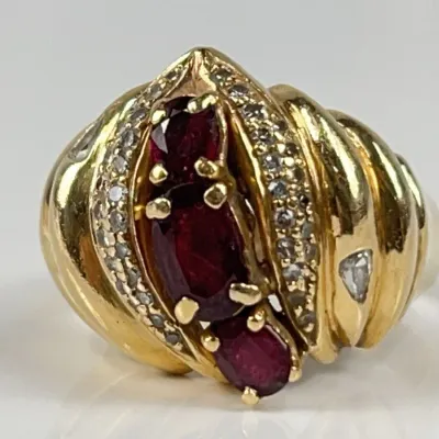 14 Kt Yellow gold statement ring featuring three oval-cut red rubies gemstones framed by diamond accents.