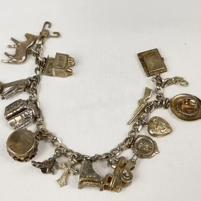 Vintage sterling silver charm bracelet featuring numerous detailed novelty charms, including a piano, cross, cowboy hat, and various...