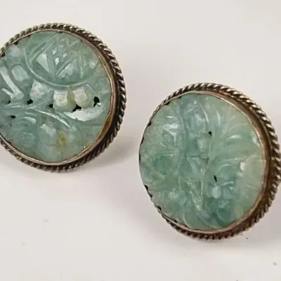 Pair of vintage round clip-on earrings featuring hand-carved light green jadeite cabochons set in Sterling Silver twisted rope bezels.