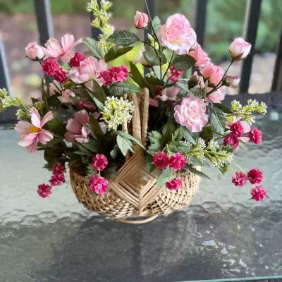 Faux pink floral arrangement set in a woven wicker basket with handles.