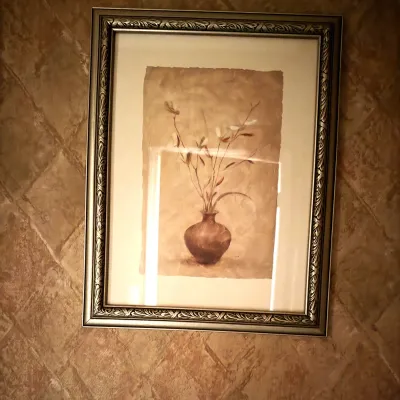 Framed wall art depicting a vase with minimal botanical branches in earth tones, set within an ornate metallic frame.