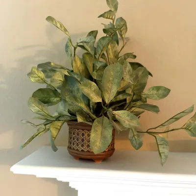 Faux leafy green plant presented in a small woven wicker and ceramic planter pot.