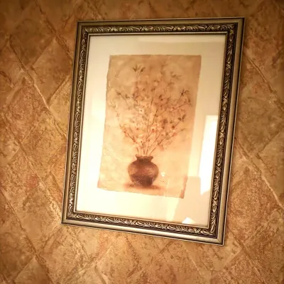 Framed wall art featuring a floral still life depiction in soft earth tones, presented in an ornate silver-and-gold carved frame.