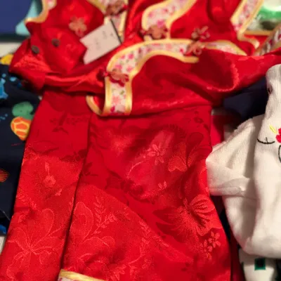 Child's red satin traditional Chinese-style outfit featuring floral jacquard fabric, pink patterned trim, and frog closure accents.