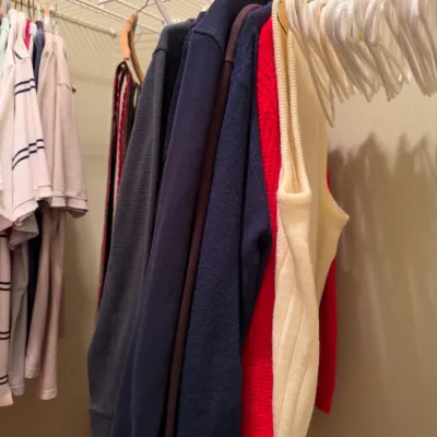 Selection of men's knit sweaters, polo shirts, and casual tops hanging in a closet.