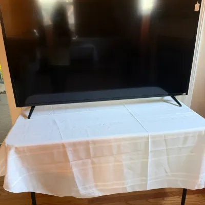Large Vizio flat-screen television with black bezel and dual legs, displayed on a covered table.