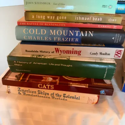 Stack of assorted hardcover and paperback books, including fiction, history, and coffee table books.