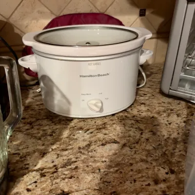 White Hamilton Beach slow cooker with a glass lid and manual control dial, in good condition on a granite countertop.