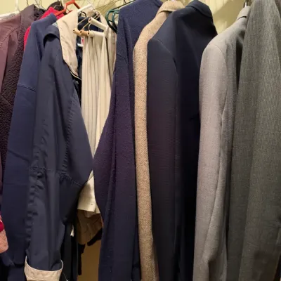 Collection of men's outerwear, suit jackets, and slacks hanging on a wire closet rack.