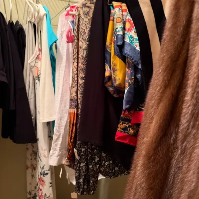 Closet filled with women's clothing, including vintage scarves, pattern dresses, tops, and a brown fur coat on hangers.