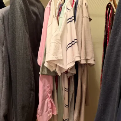 Closet full of men's clothing, including suit jackets, long-sleeve dress shirts, polo shirts, and neckties on hangers.