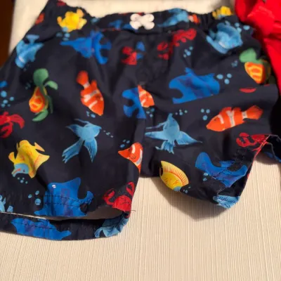 Child's dark blue swim trunks featuring a colorful ocean sealife pattern, including fish, turtles, and crabs.