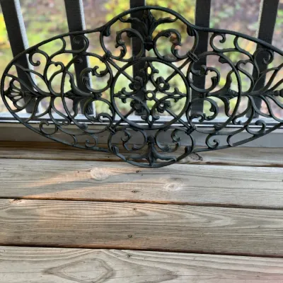 Black cast iron decorative wall or garden plaque featuring intricate scrollwork and floral motifs.