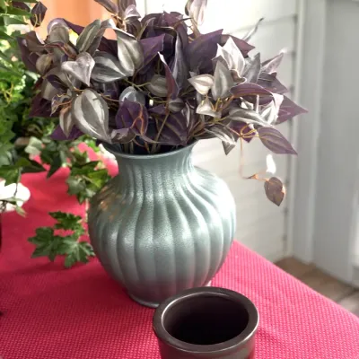 Faux purple tradescantia arrangement in a ribbed metallic light blue vase, displayed alongside a small ceramic pot.