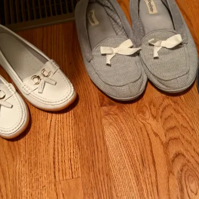 Two pairs of women's shoes including white leather loafers with gold hardware detail and grey Dearfoams cloth slippers with white...