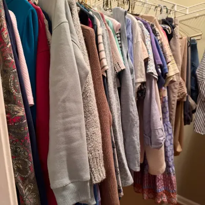 Closet rack filled with a variety of women's clothing including sweaters, shirts, and dresses.