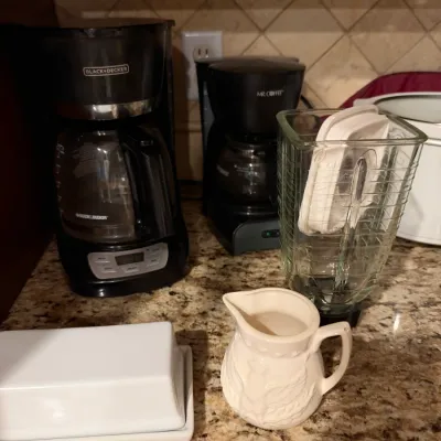 Collection of small kitchen appliances including a Black + Decker coffee maker, a Mr. Coffee maker, a blender jar, a white ceramic cream...