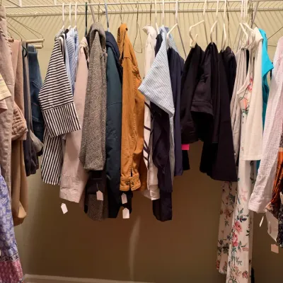 Closet rack filled with contemporary women's clothing, including jackets, blouses, and dresses, alongside a pair of white loafers...