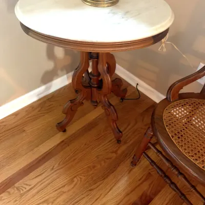 Victorian-style round parlor table featuring a white marble top and carved wooden pedestal base with casters.
