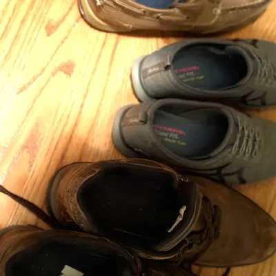 Selection of men's casual footwear on a hardwood floor, including grey Skechers Relaxed Fit memory foam sneakers, brown leather work...