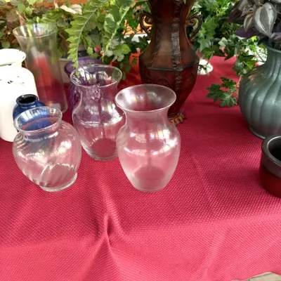 Collection of assorted glass and ceramic flower vases displayed alongside artificial greenery on a table.