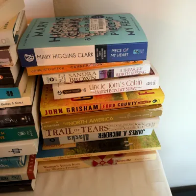 Stack of assorted paperback and hardcover fiction and non-fiction books, including titles by Mary Higgins Clark, John Grisham, and James...