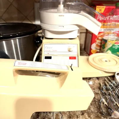 Vintage Oster Kitchen Center appliance base with food processor attachment, mixer head, and chrome beaters.