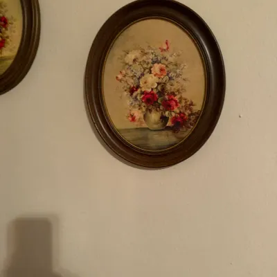 Vintage framed oval wall art depicting a still life floral arrangement in a vase, housed in a dark wooden frame.