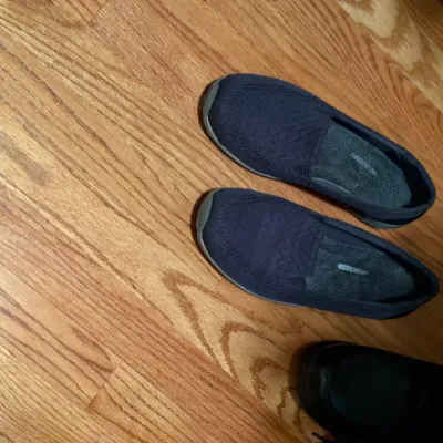 Pair of women's navy blue knit slip-on shoes with patterned insoles resting on a hardwood floor.