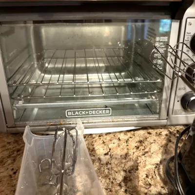 Black+Decker countertop toaster oven with a glass door and wire rack, shown alongside electric hand mixer attachments.