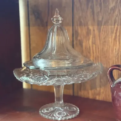 Sale Photo Thumbnail #178: Vintage clear pressed glass pedaled pedestal candy dish with a matching domed lid, displaying intricate pattern details on the rim and base.