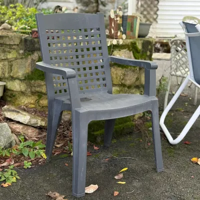 Sale Photo Thumbnail #209: Dark gray molded plastic patio armchair featuring a lattice-pattern backrest, placed outdoors on an asphalt driveway.