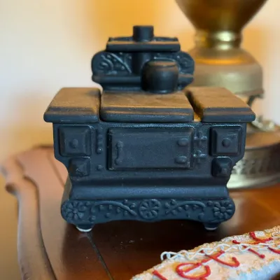Sale Photo Thumbnail #81: Vintage black matte ceramic or cast iron miniature potbelly stove figurine featuring embossed scrollwork and a raised cooktop detail.