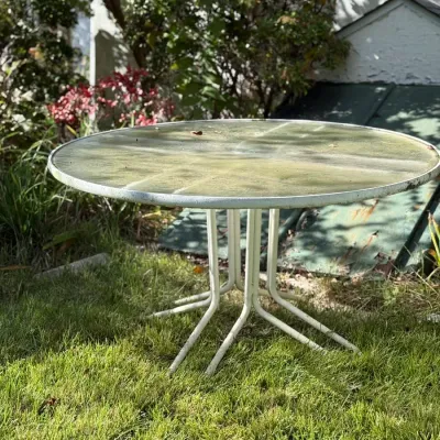Sale Photo Thumbnail #248: Round vintage outdoor patio table featuring a painted white metal frame with a glass top, set on a grassy lawn.