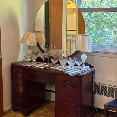 Sale Photo Thumbnail #41: Vintage dark mahogany vanity desk with a large round attached mirror, featuring various glassware and small table lamps displayed on top.