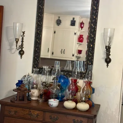 Sale Photo Thumbnail #4: Collection of vintage oil and kerosene lamps displayed atop a dark oak dresser beneath a carved wall mirror and matching sconces.