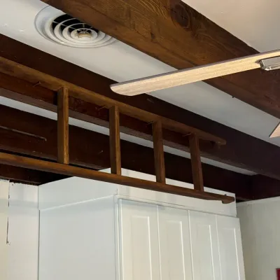 Sale Photo Thumbnail #105: Vintage wooden ladder mounted horizontally as overhead decorative storage or display above white cabinetry.