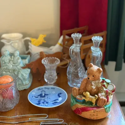 Sale Photo Thumbnail #73: Assortment of vintage knick-knacks including a teddy bear music box, cut glass decanters, blue decorative plate, ceramic figurines, and wire kitchen tools.